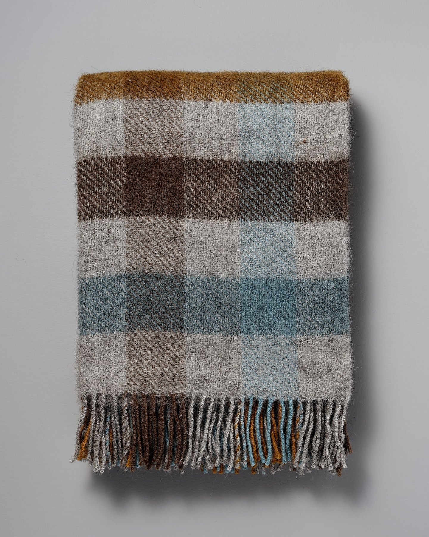 A Gotland Wool Throw – Multi Turquoise with fringes on a white background.