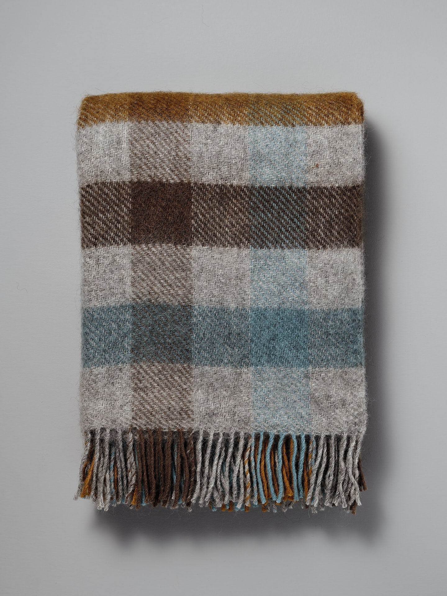A Gotland Wool Throw – Multi Turquoise with fringes on a white background.