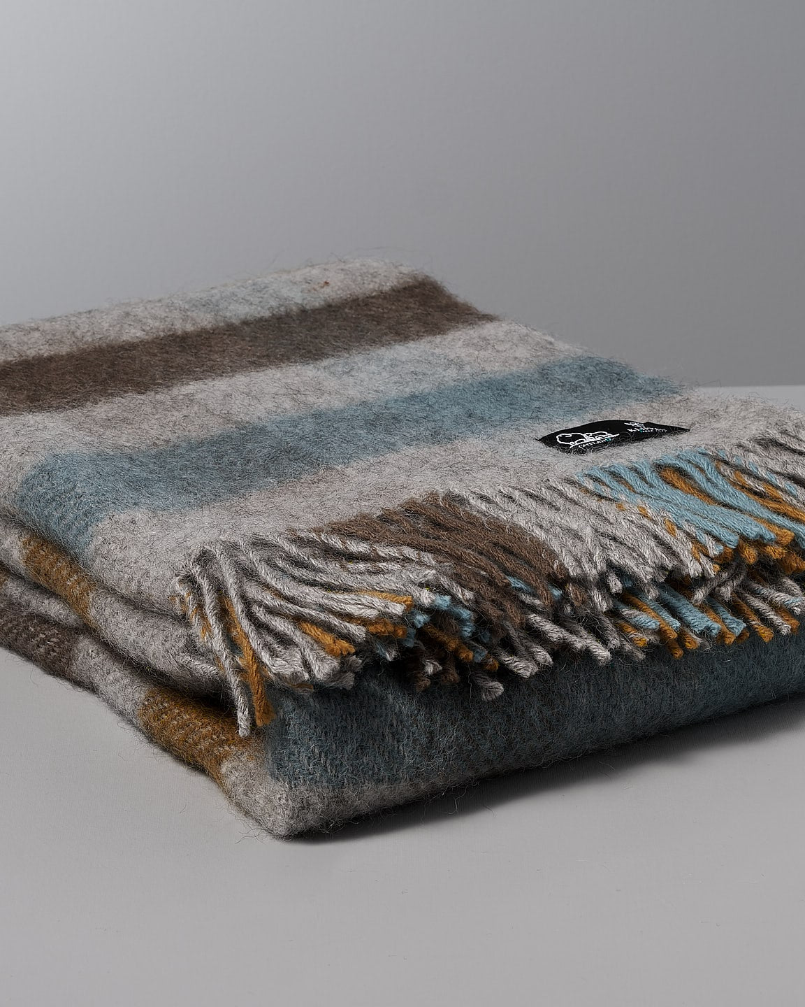 A Gotland Wool Throw – Multi Turquoise with fringes on a white background.