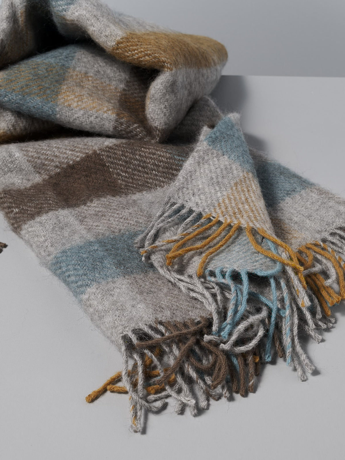 A Klippan Gotland Wool Throw – Multi Turquoise blanket with fringes.