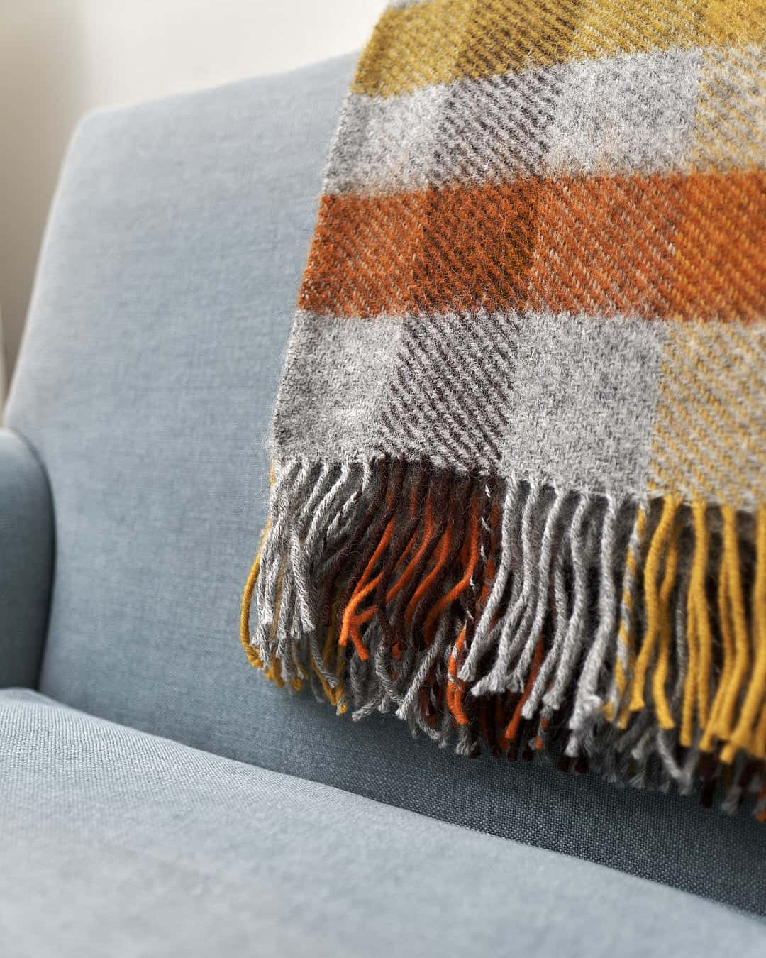 A Klippan Gotland Wool Throw – Multi Yellow on a couch in a living room.