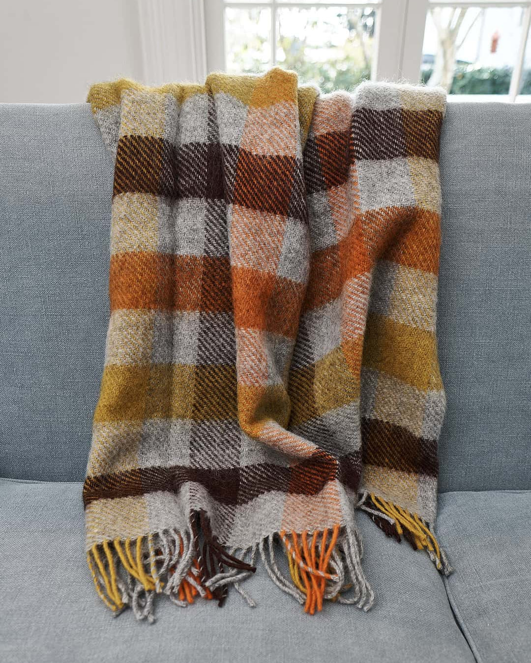 A Klippan Gotland Wool Throw – Multi Yellow on a couch in a living room.