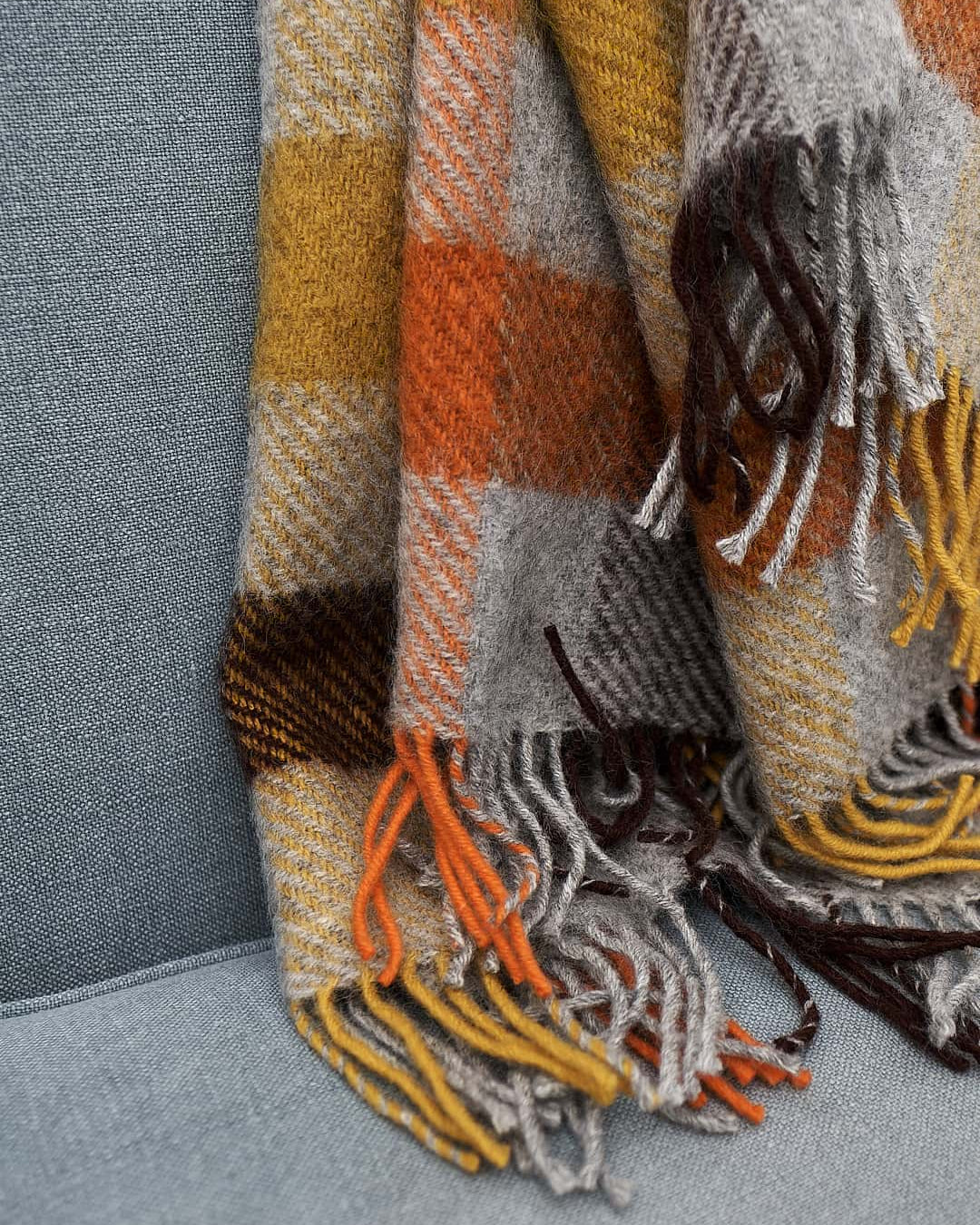 A Gotland Wool Throw – Multi Yellow with fringes on a couch by Klippan.