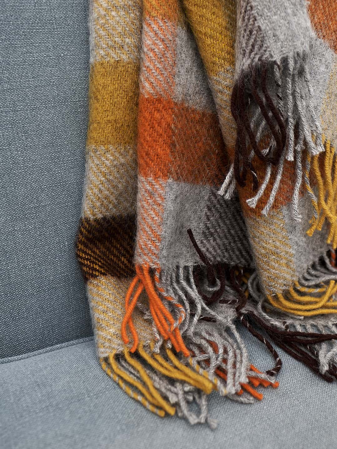 A Gotland Wool Throw – Multi Yellow with fringes on a couch by Klippan.