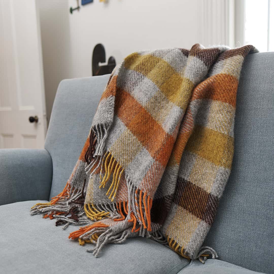 A Gotland Wool Throw – Multi Yellow by Klippan on a couch in a living room.