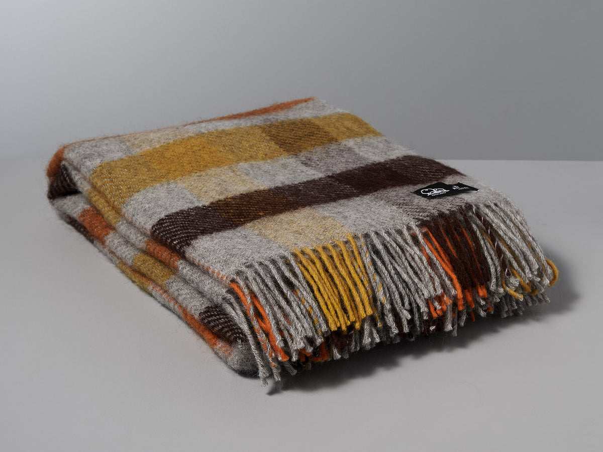 A brown, orange and yellow Klippan Gotland Wool Throw – Multi Yellow blanket on a white surface.