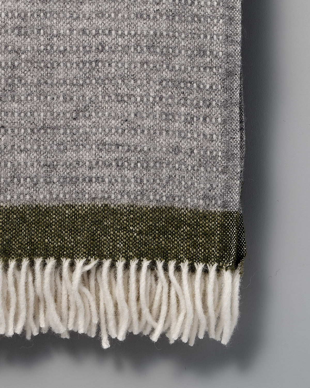 A Klippan Hampus Wool Throw - Grey Green with fringes on a white background.