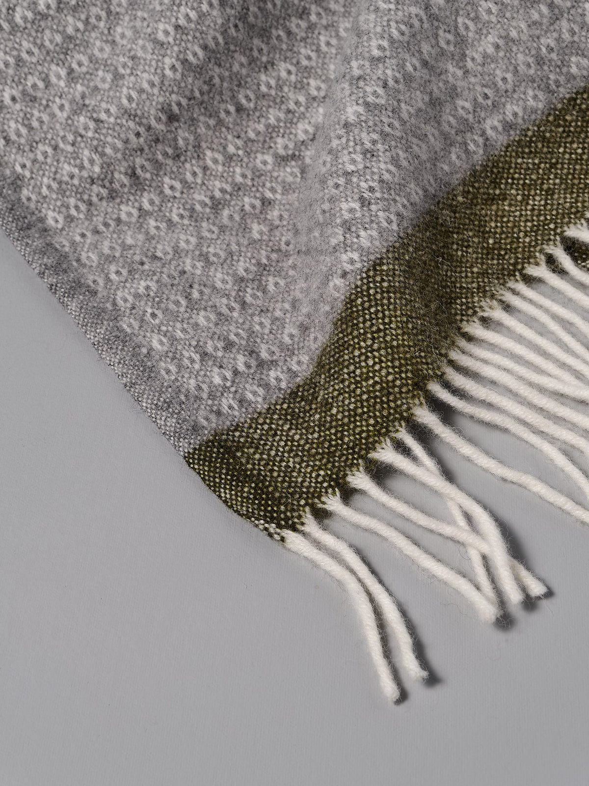 A Klippan Hampus Wool Throw – Grey Green with fringes.