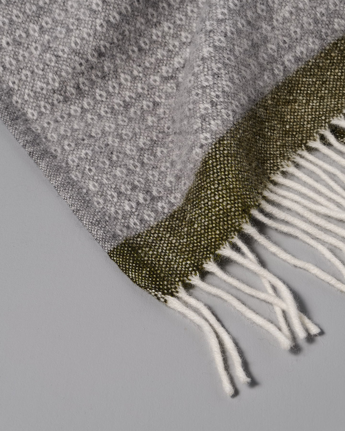A Klippan Hampus Wool Throw – Grey Green with fringes.