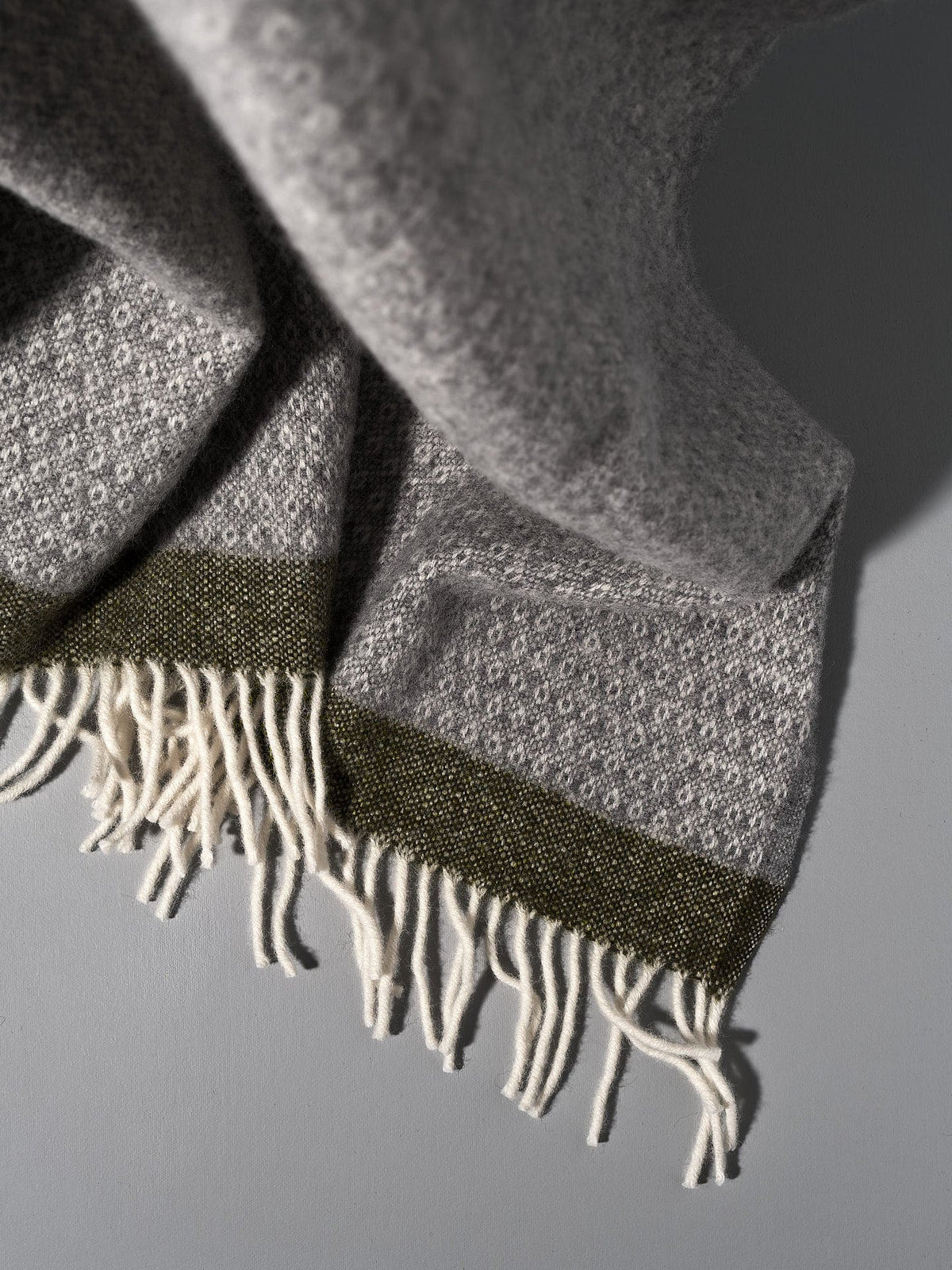 A Klippan Hampus Wool Throw – Grey Green with fringes.