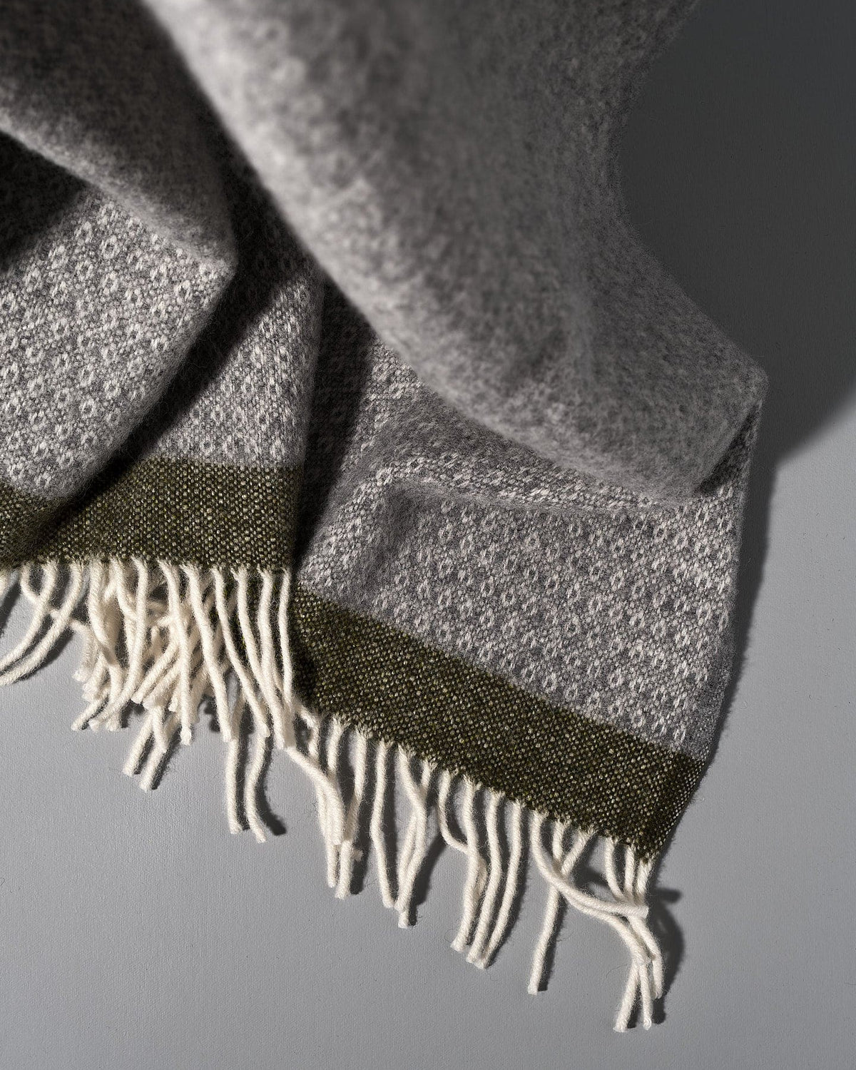 A Klippan Hampus Wool Throw – Grey Green with fringes.