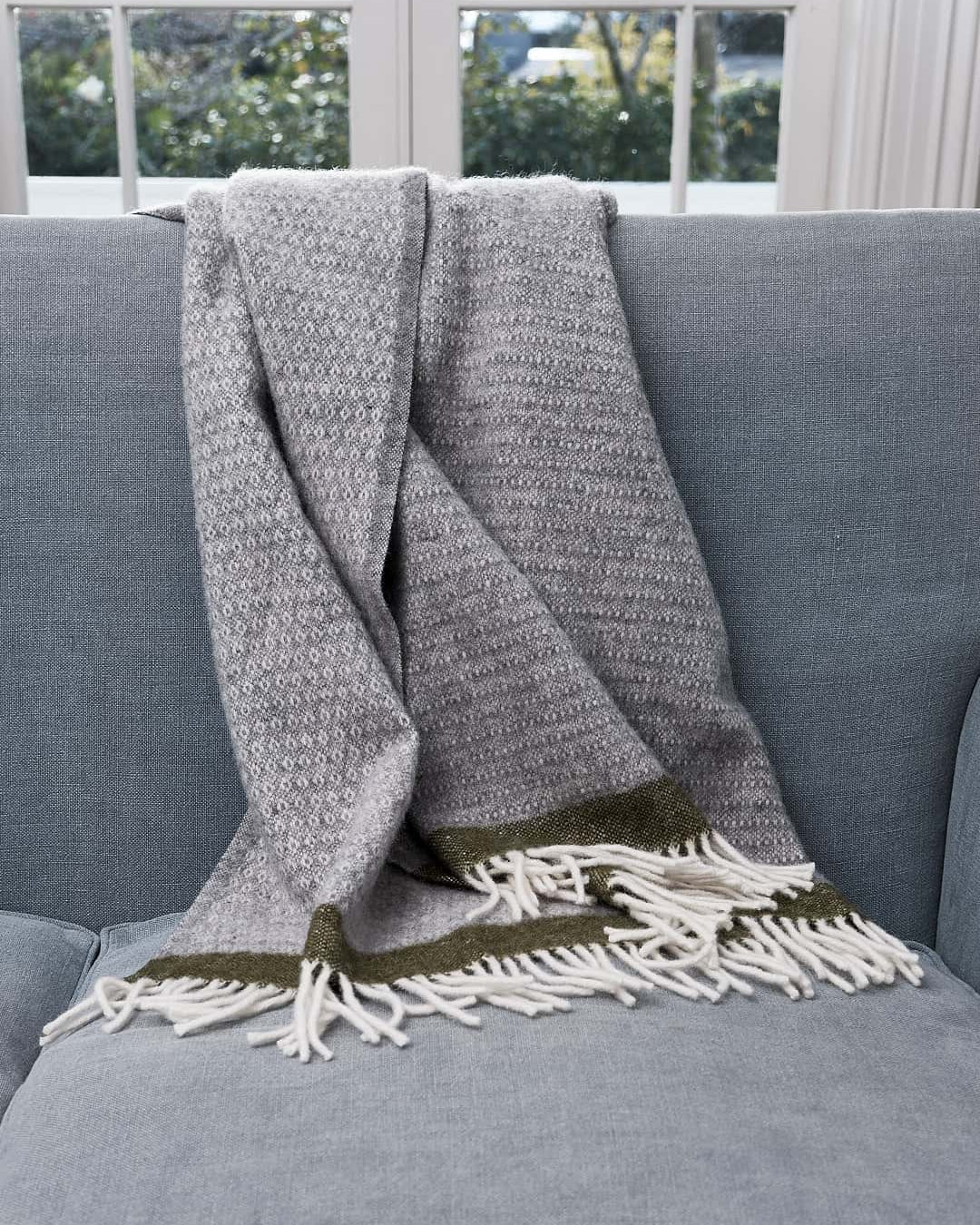 A Hampus Wool Throw – Grey Green by Klippan on a couch.