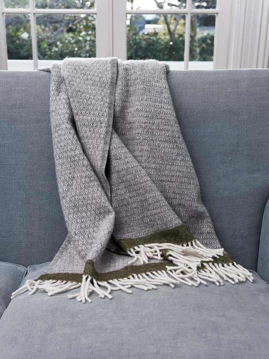 A Hampus Wool Throw – Grey Green by Klippan on a couch.