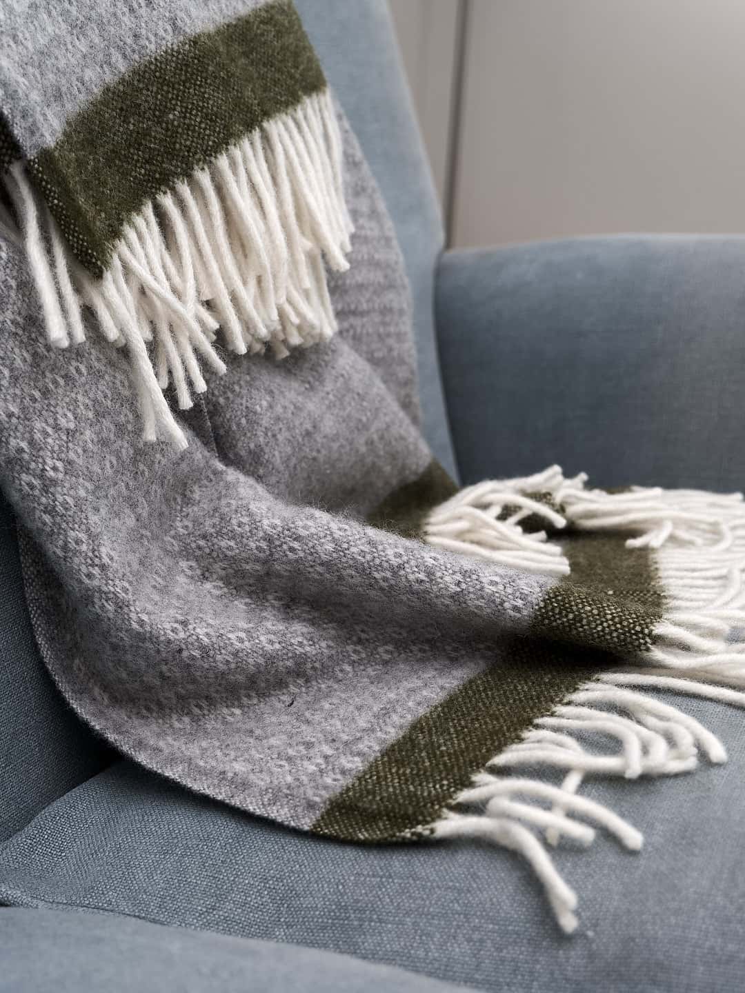 A Hampus Wool Throw - Grey Green by Klippan on a couch.