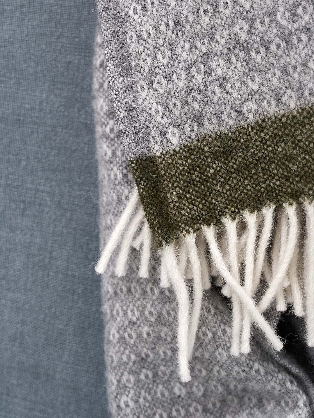 A close up of a Klippan Hampus Wool Throw – Grey Green blanket with fringes.