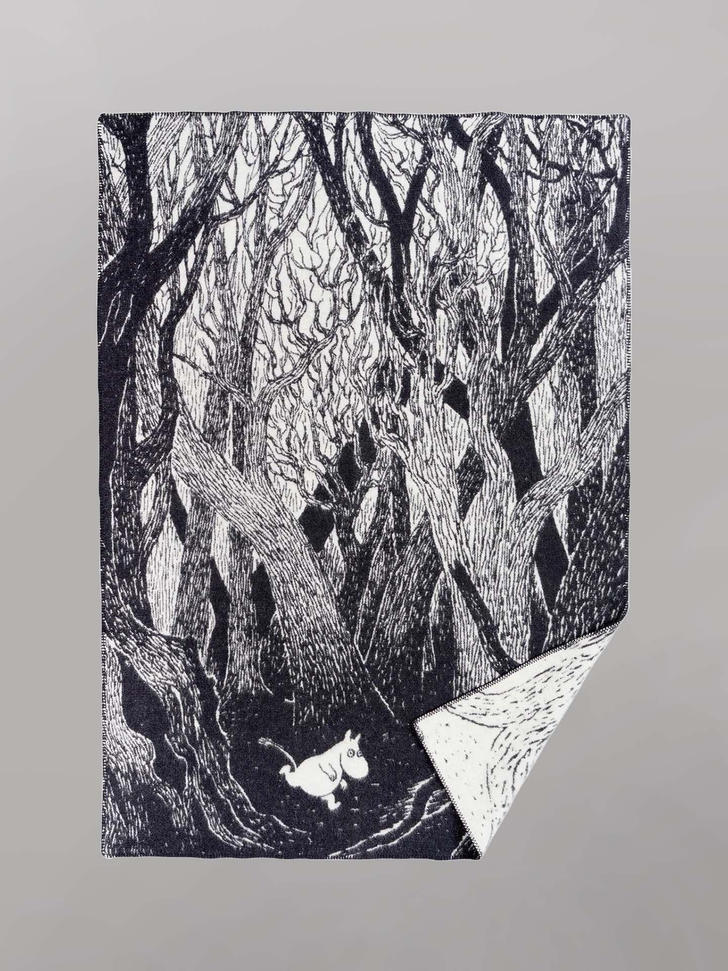 A black and white Klippan Moomin on the Run Blanket featuring an illustration of dense, intertwined trees in a forest with a small white creature walking along the forest floor. This eco-friendly children's blanket is crafted from organic lambswool, ensuring both comfort and sustainability.