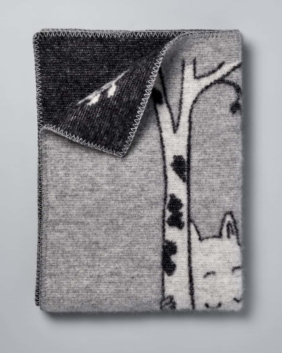 A grey and black Moomin Baby Blanket – Tree Hug with a cat on it. (Brand Name: Klippan)