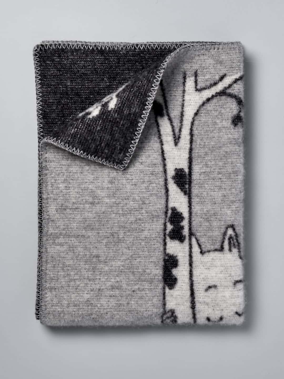 A grey and black Moomin Baby Blanket – Tree Hug with a cat on it. (Brand Name: Klippan)