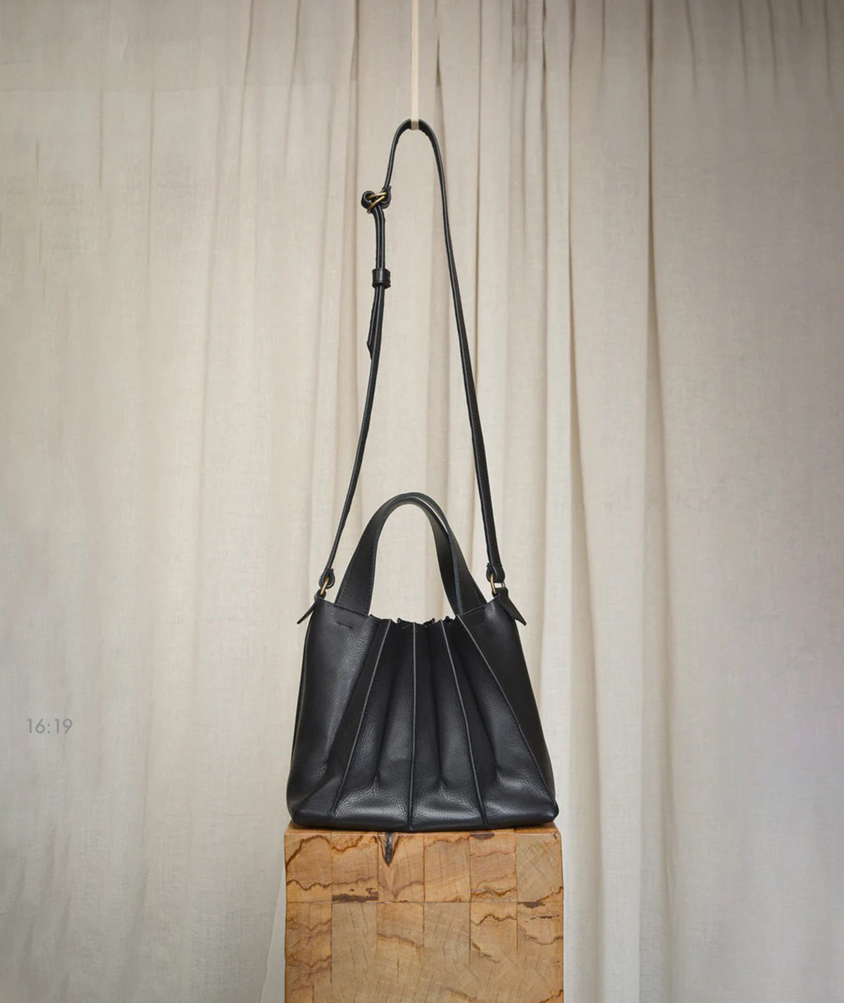 A Pleats Petite cowhide leather handbag hanging on a wooden block by Kohl &amp; Co.
