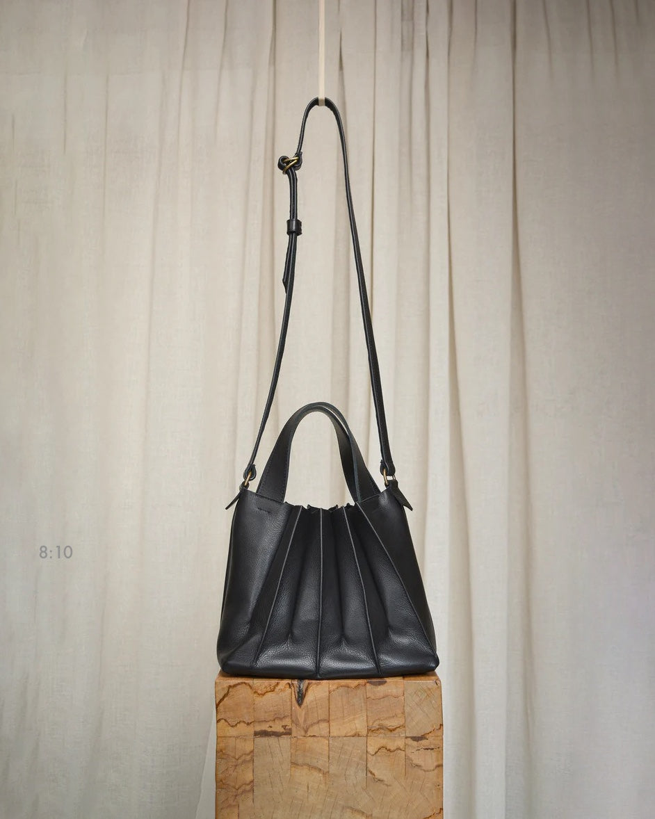 A Pleats Petite handbag by Kohl &amp; Co, made of black cowhide leather, sitting on top of a wooden block.