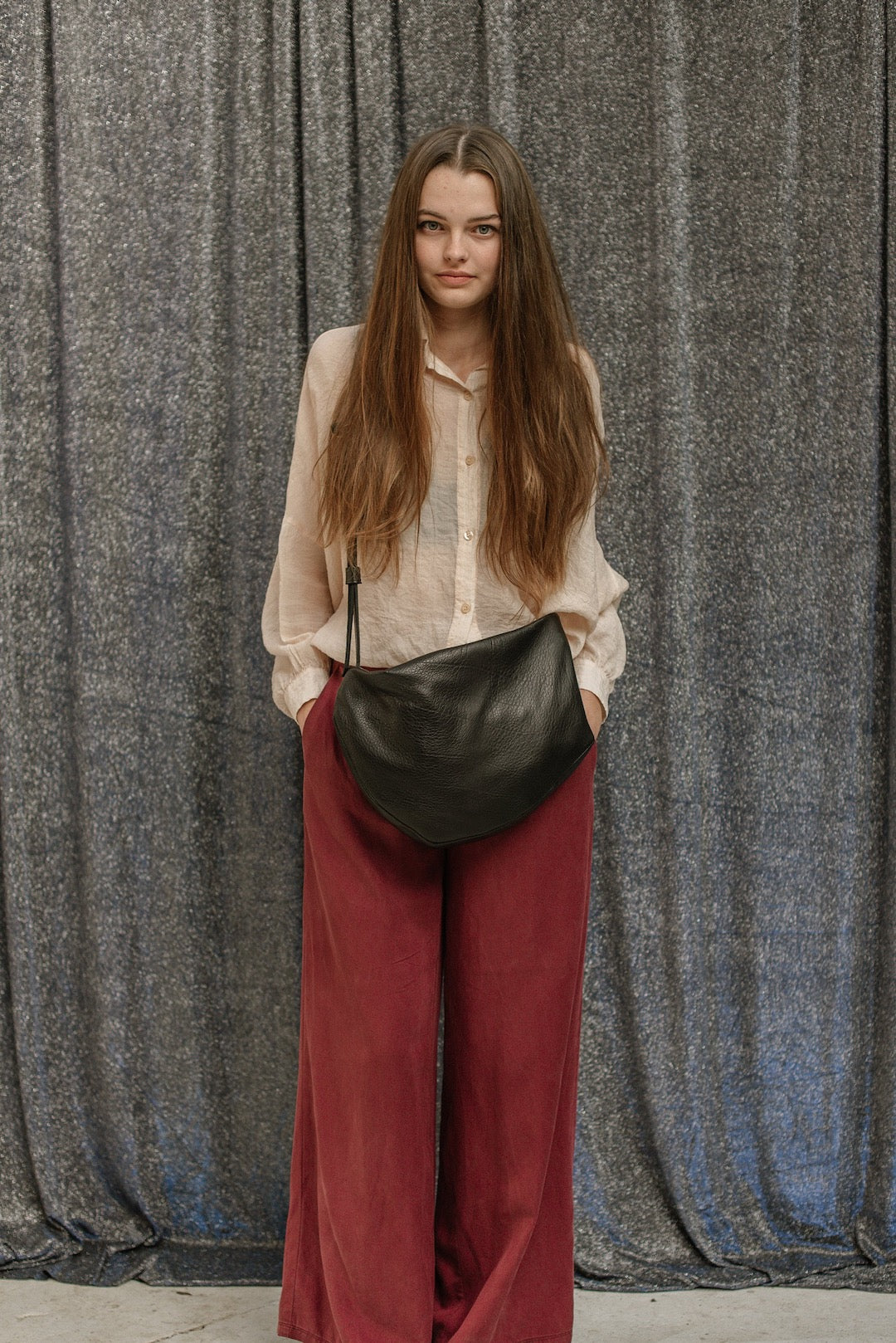 A woman in burgundy wide leg pants and a black Side Saddle purse from Kohl &amp; Co.