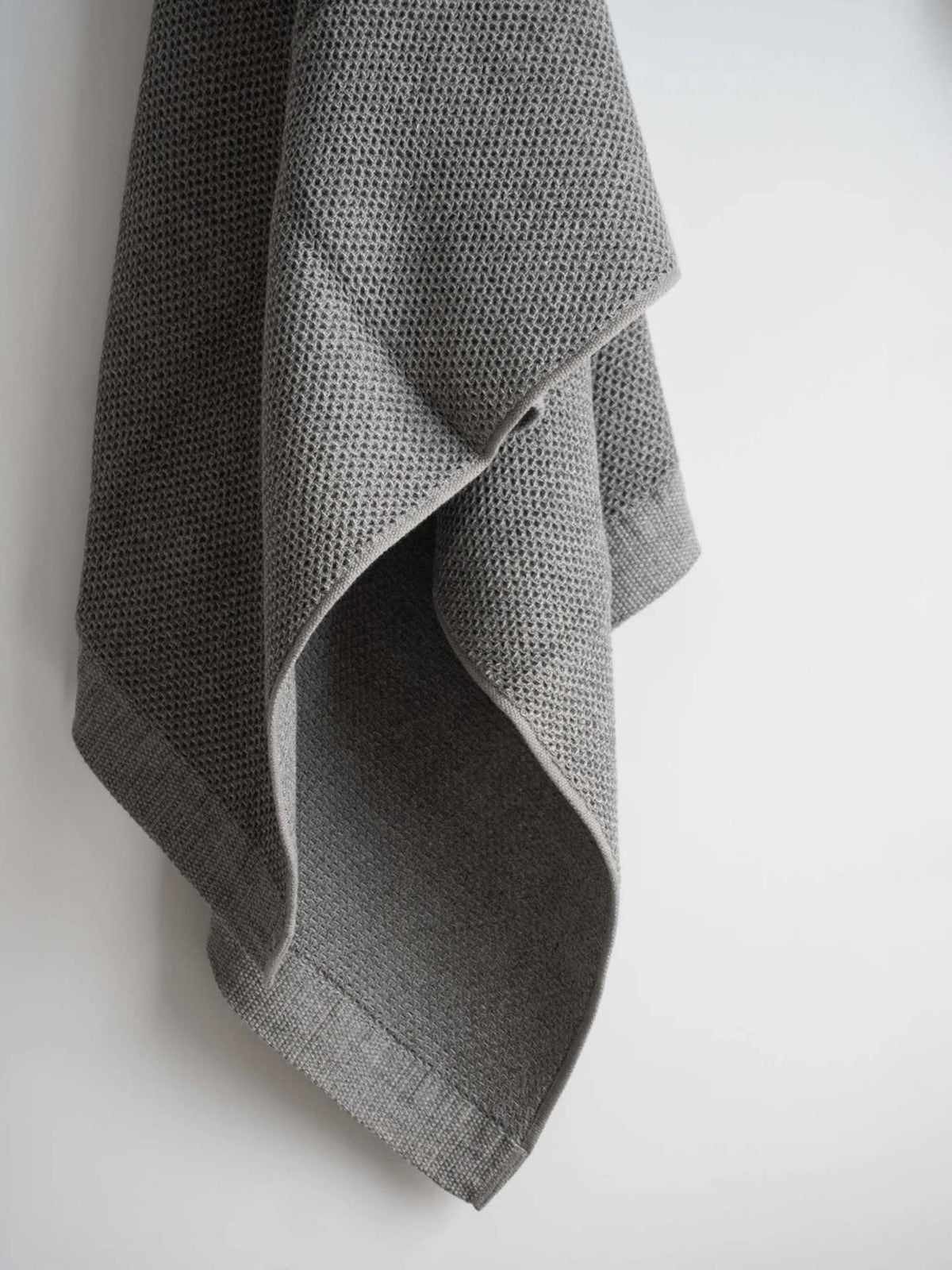 A Kontex Vintage Waffle Towel in gray, famed for its quick-drying capability, hangs elegantly against a pristine white background.