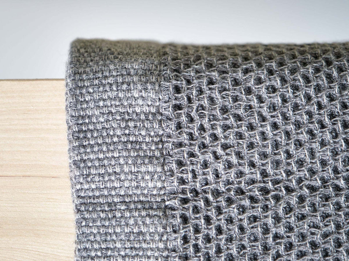 A close-up of a Vintage Waffle Towel by Kontex, crafted from gray waffle knit cotton and linen, draped elegantly over the edge of a wooden surface.