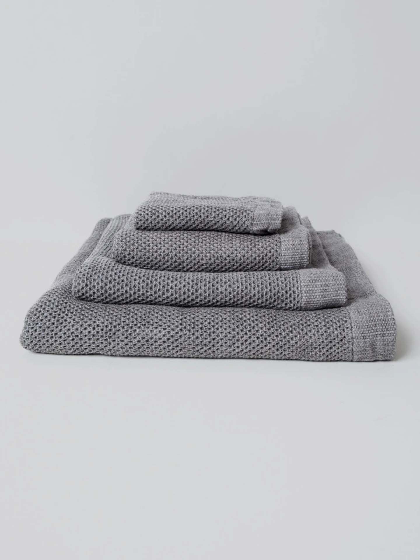 A neatly arranged set of Kontex's Vintage Waffle Towels – Bath ⋄ Hair ⋄ Hand ⋄ Face, featuring a luxurious gray waffle texture and fast-drying performance, is elegantly displayed against a plain white background.