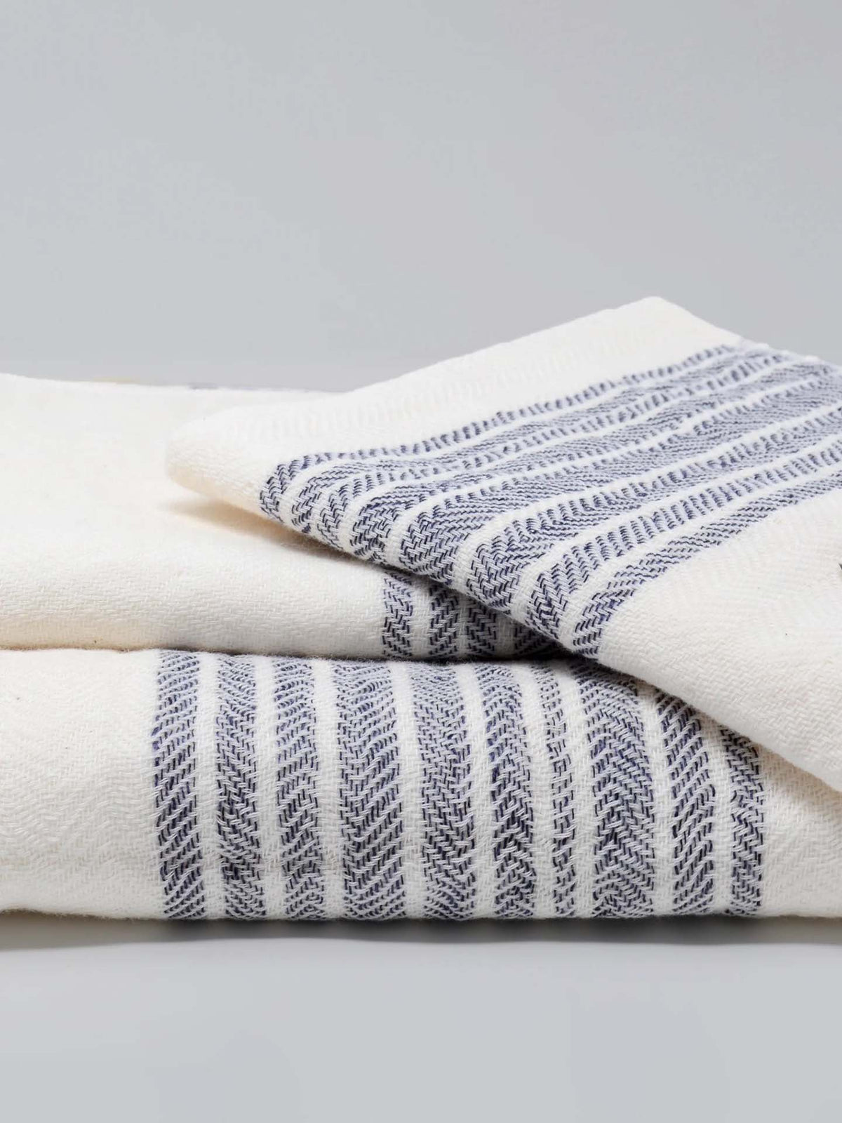 A pair of Kontex Flax Line Organic Towels, featuring blue stripes on a white background and made from 100% organic cotton, are neatly stacked on a flat surface.