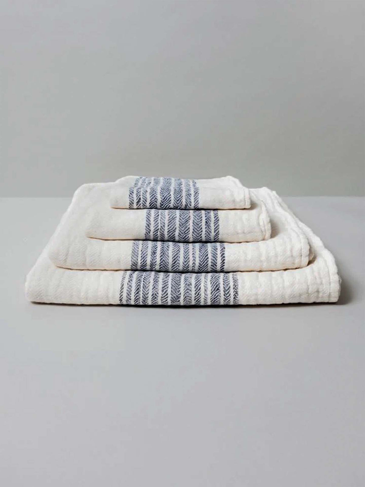 A set of Flax Line Organic Towels by Kontex, featuring blue stripes and made from organic cotton, are neatly stacked on a plain surface.