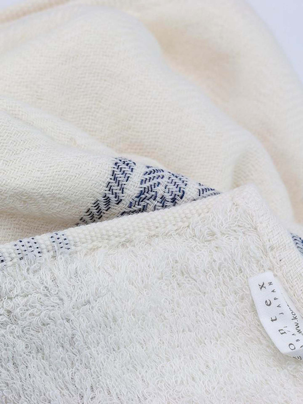 Close-up of a folded white and blue woven textile from Kontex&#39;s Flax Line Organic Towel collection, crafted with organic cotton, featuring a visible label.