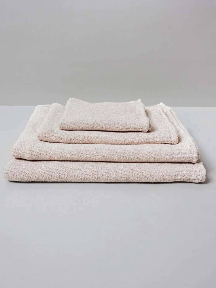 A neatly stacked set of three Kontex Re.Lana Towels from their Bath ⋄ Hair ⋄ Hand ⋄ Face collection, crafted from recycled cotton in beige hues, rests on a gray surface.