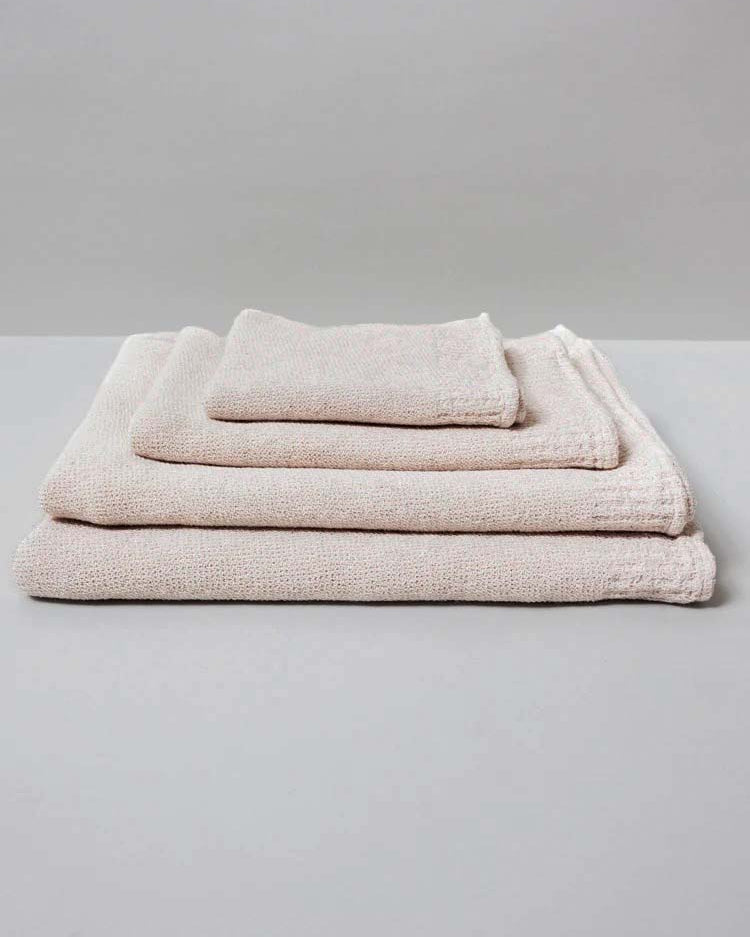 A neatly stacked set of three Kontex Re.Lana Towels from their Bath ⋄ Hair ⋄ Hand ⋄ Face collection, crafted from recycled cotton in beige hues, rests on a gray surface.