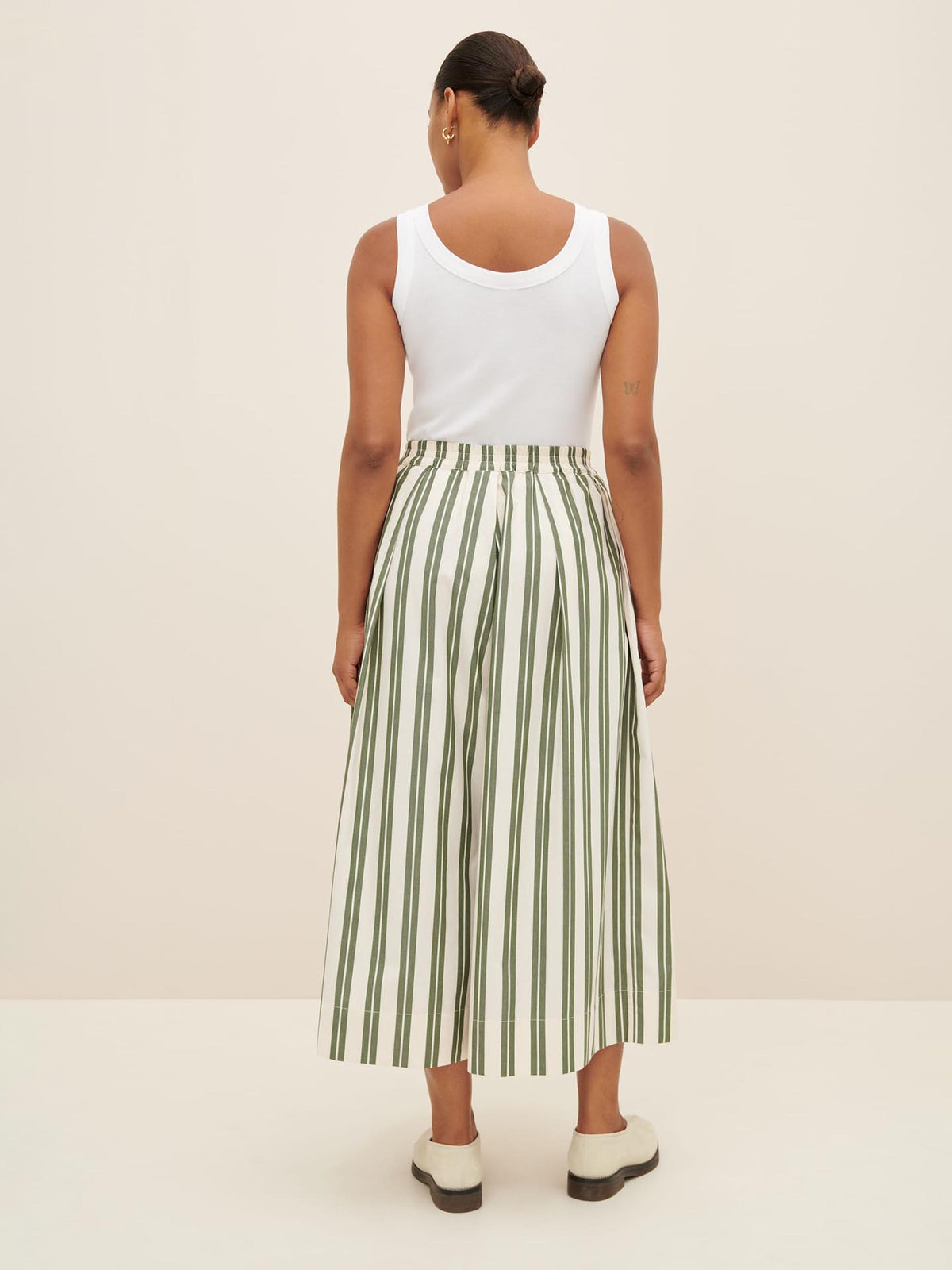 Person in a white sleeveless top and the Athena Pant – Forest Stripe by Kowtow, featuring high-waisted green and white striped wide-leg pants with a relaxed fit, photographed from behind against a plain background. Consider checking the size guide if you need to size down.