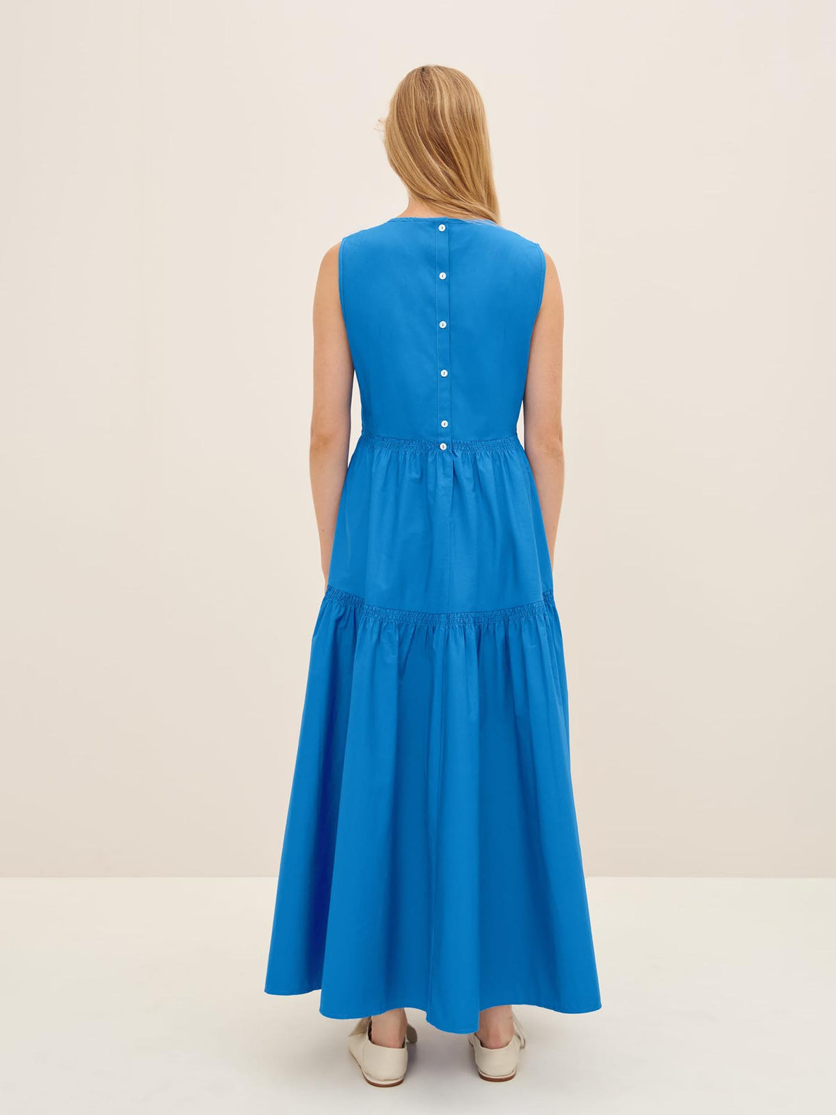 A person with long hair is wearing the Aurora Dress by Kowtow in size XS, featuring a row of buttons on the back, and is standing in a light-colored room.