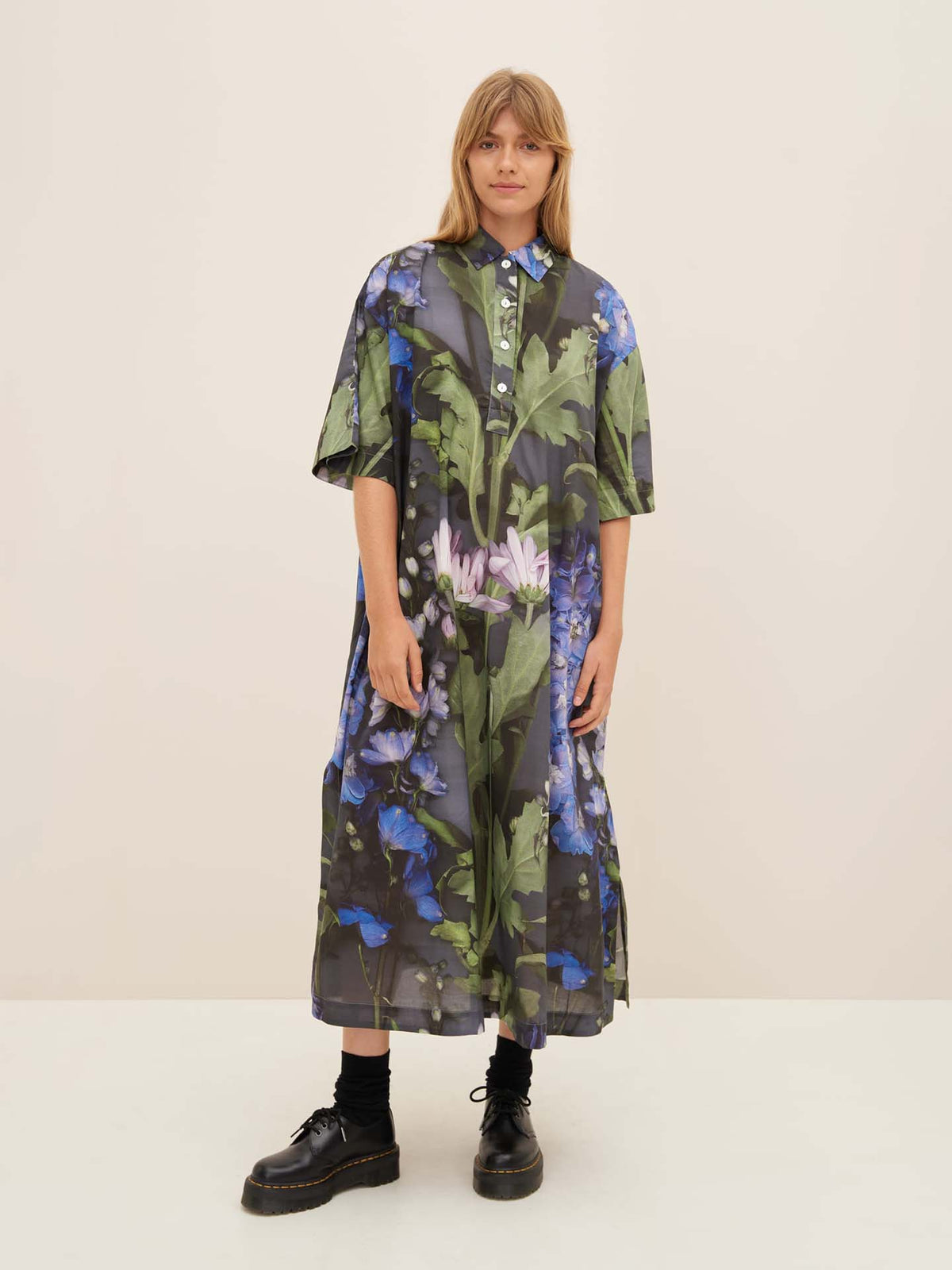 A person wearing the Bloom Dress by Kowtow, a long floral garment with a collared design and standard fit, stands against a light background.