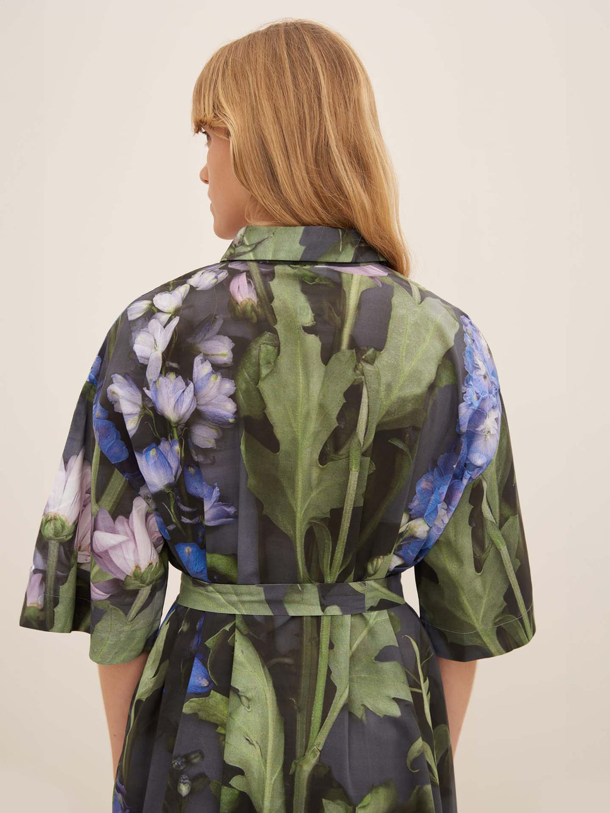 A person with long light brown hair is seen from the back wearing the Bloom Dress by Kowtow, which features a large floral garment pattern.