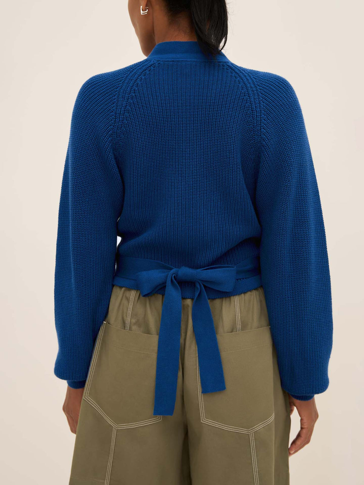 Individual wearing an oversized Composure Cardigan in Primary Blue from Kowtow along with khaki pants, seen from the back.