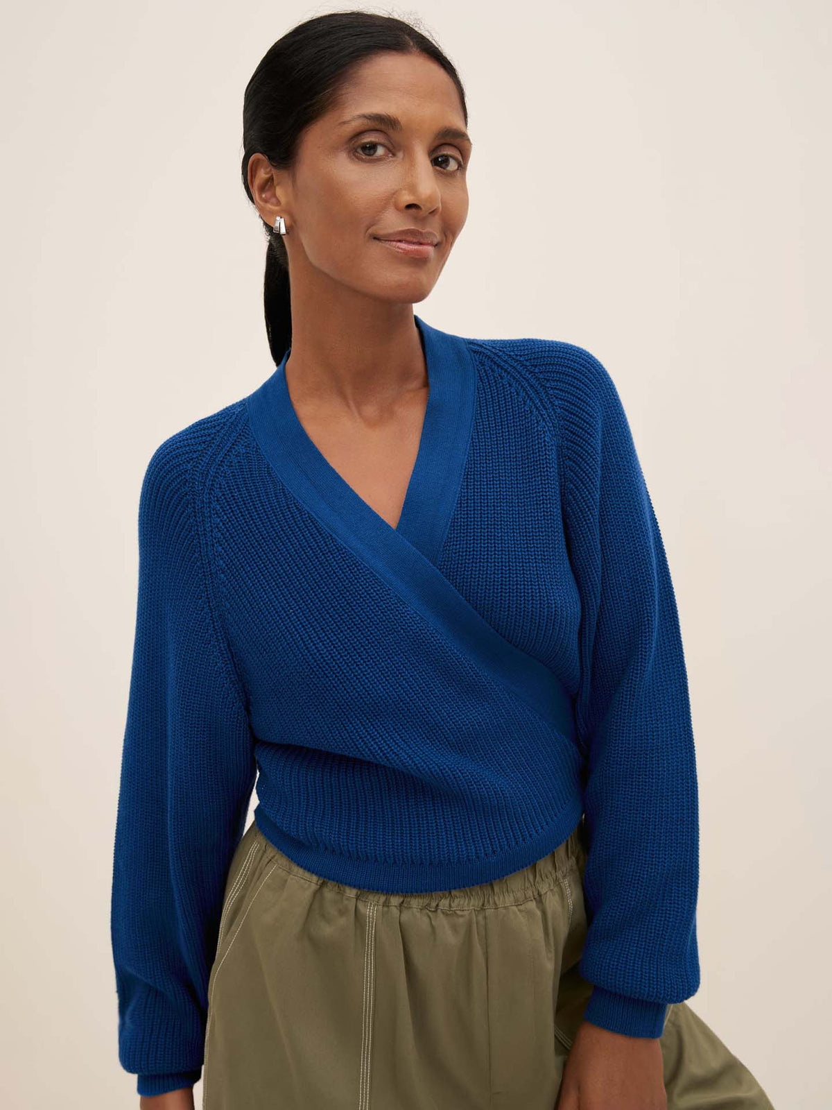 A person wearing the Kowtow&#39;s Composure Cardigan in primary blue and olive green pants, standing against a plain background.