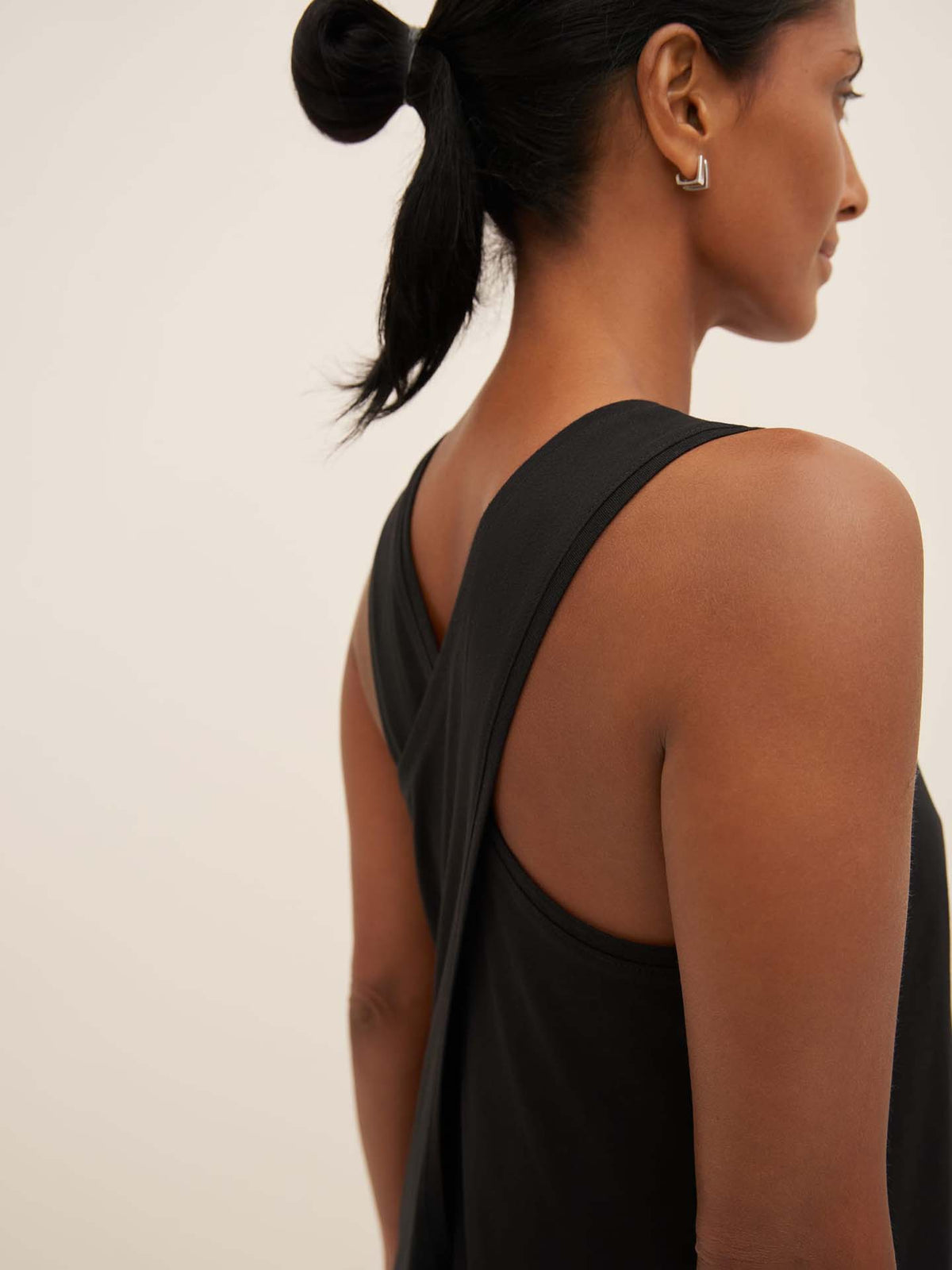 A person wearing the Cross Back Dress in black by Kowtow, seen from the side, perfectly showcases the standard fit.