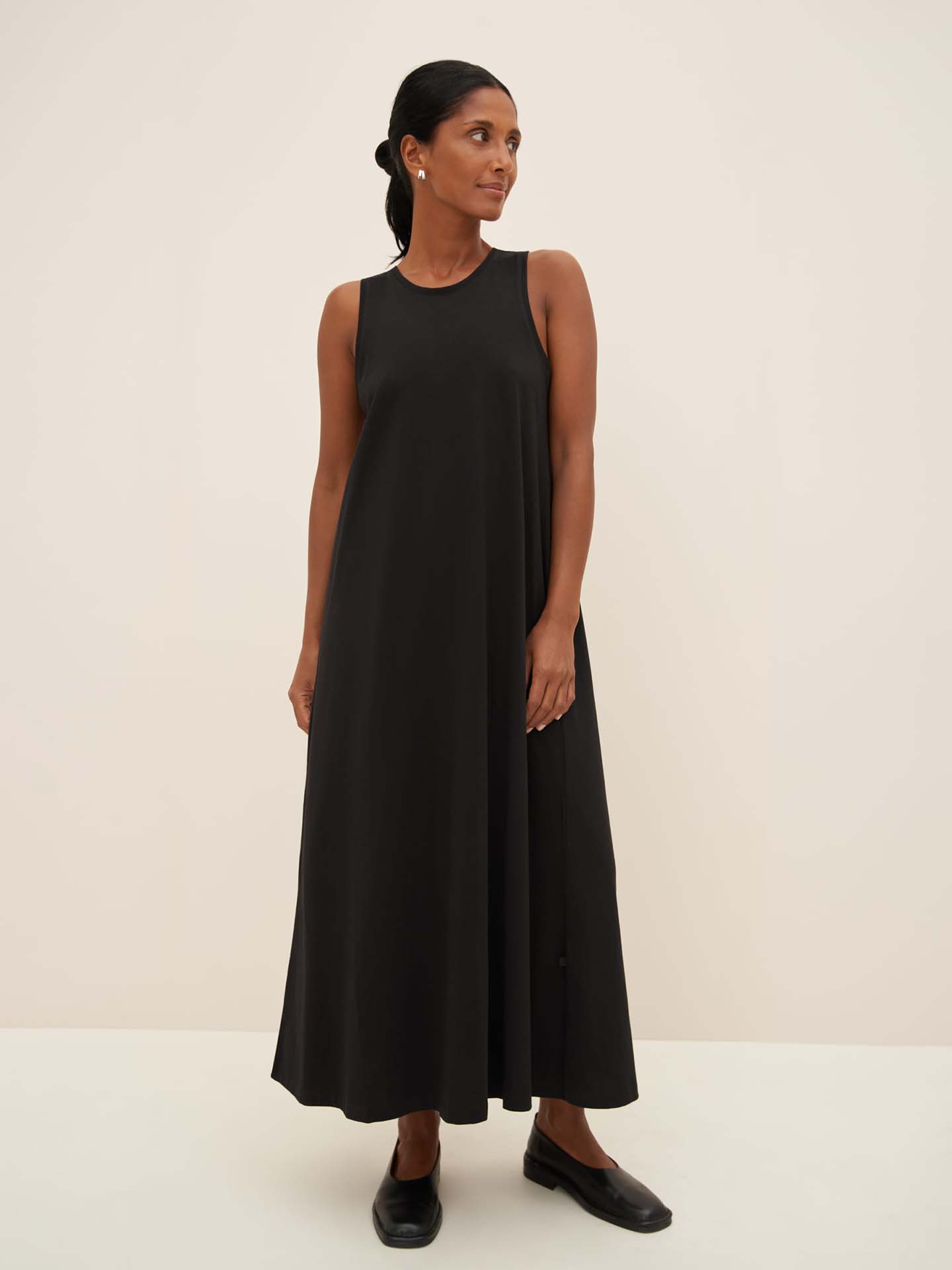 A person wearing a Kowtow Cross Back Dress in black and matching black shoes stands against a plain background, highlighting the standard fit of the garment.