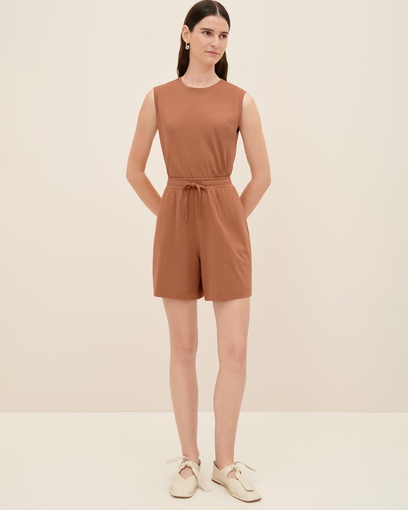 A woman stands against a plain background wearing the Drawcord Shorts in Sienna from Kowtow and cream-colored shoes. She has long hair and is looking directly at the camera, with her arms relaxed by her sides. Consult our size guide for the perfect fit.