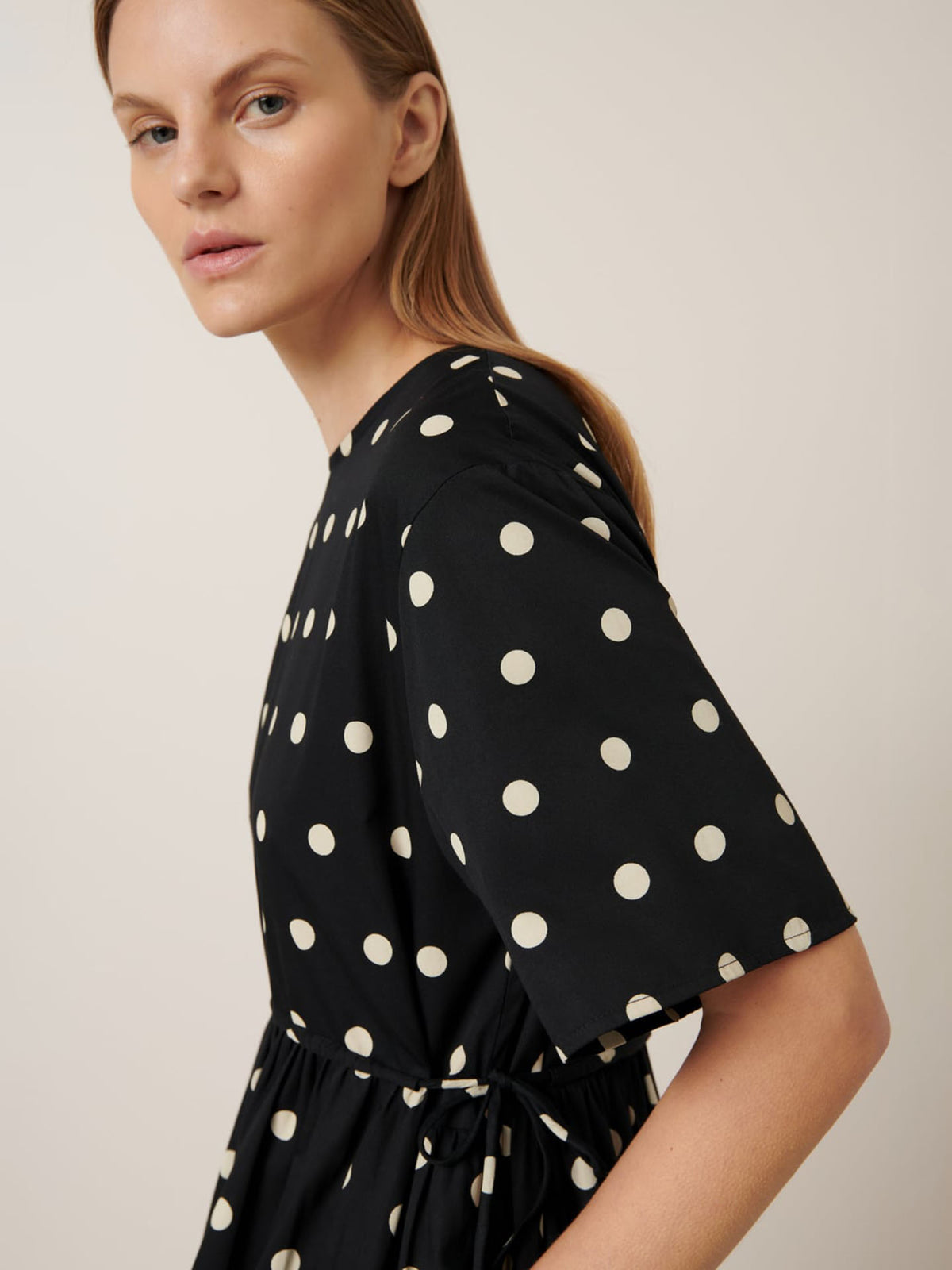 Wearing the Eclipse Dress – Polka Dot by Kowtow, a person gazes sideways with a neutral expression.