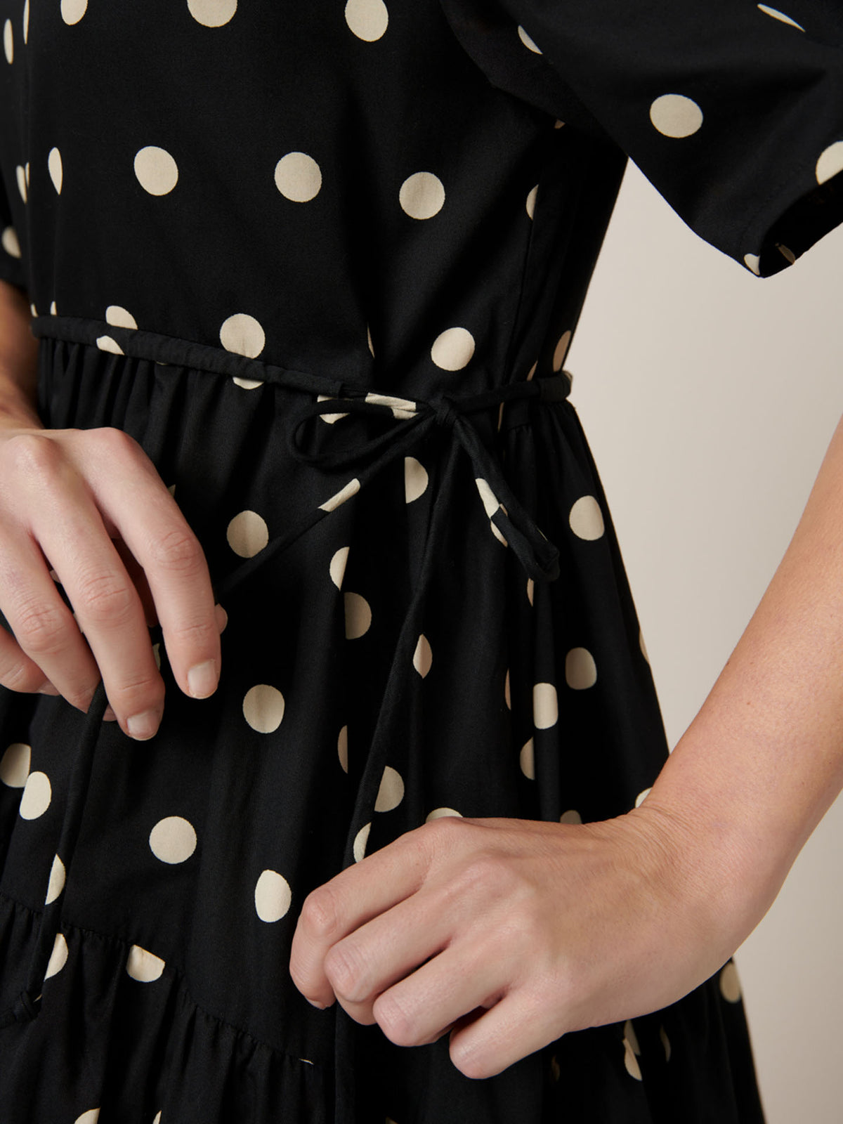 A close-up shows hands tying the waist belt of Kowtow&#39;s Eclipse Dress – Polka Dot, offering elegance and comfort with every movement.