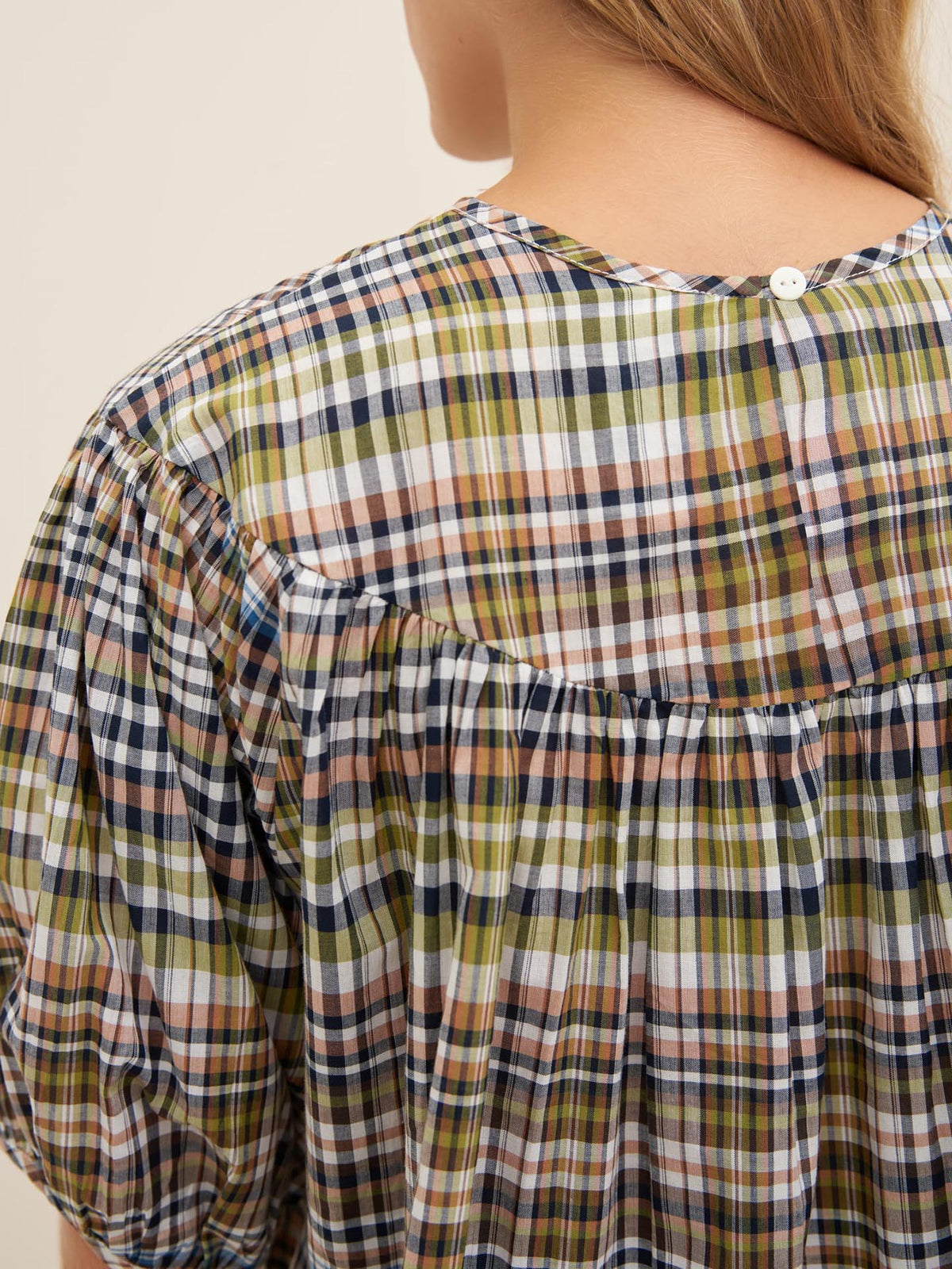 A person with long hair is seen from the back wearing the Frances Top by Kowtow, which features a multicolored, plaid pattern and an oversized fit.