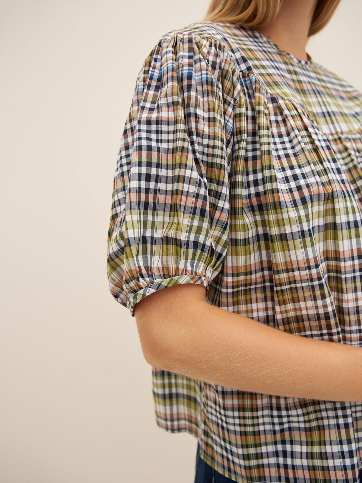 A person is wearing the Frances Top by Kowtow, which features a multicolored plaid pattern, short puffed sleeves, and an oversized fit.