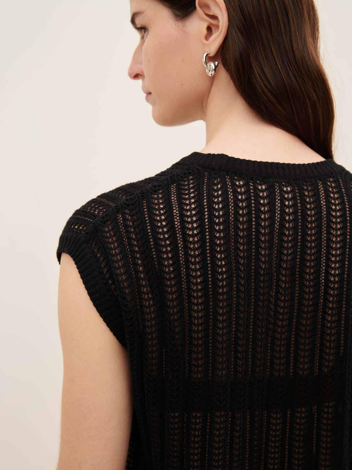 A person with long, dark hair is seen from the back wearing the Kowtow Komorebi Singlet, a stylish sleeveless knit top with a vertical striped pattern, complemented by silver earrings. Ideal for those referencing the Kowtow size guide for a standard fit.