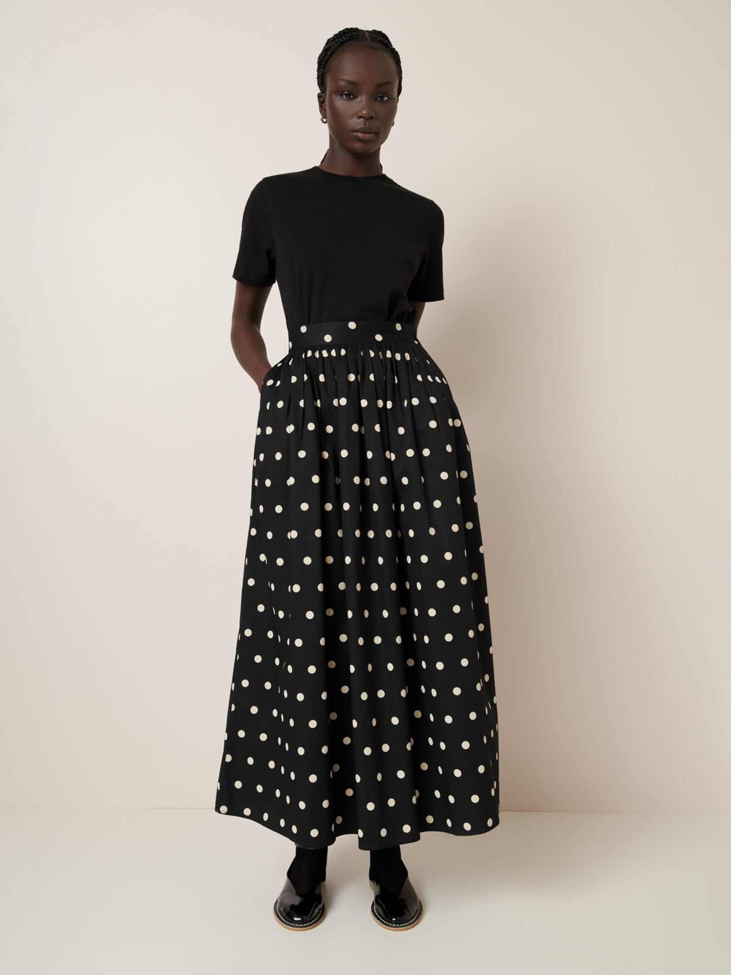 Dressed in the Kowtow black t-shirt and Luna Skirt – Polka Dot, a person with a relaxed-fit silhouette stands against a plain background.