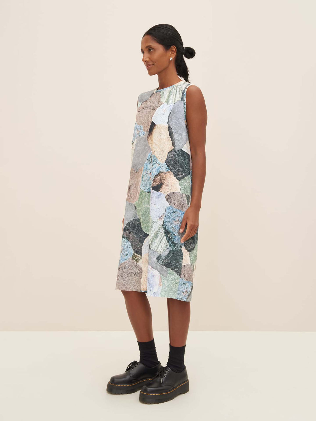 A person wearing the Mineral Singlet Dress by Kowtow stands against a plain background, facing slightly to the left. The sleeveless multicolored dress offers a close fit paired with black shoes and socks, perfectly highlighting the garment&#39;s unique measurements.