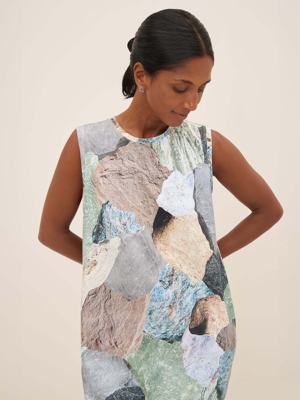 A person in a Mineral Singlet Dress by Kowtow, featuring a vibrant rock pattern, stands against a plain background. The dress is tailored with precision to fit perfectly as the wearer looks down.